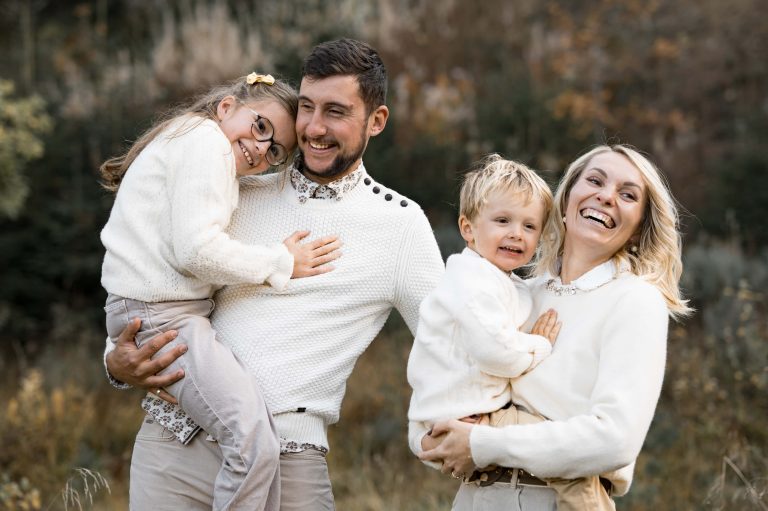 Photographie d'une famille s'enlaçant. Ils sont en forêt et sourient.