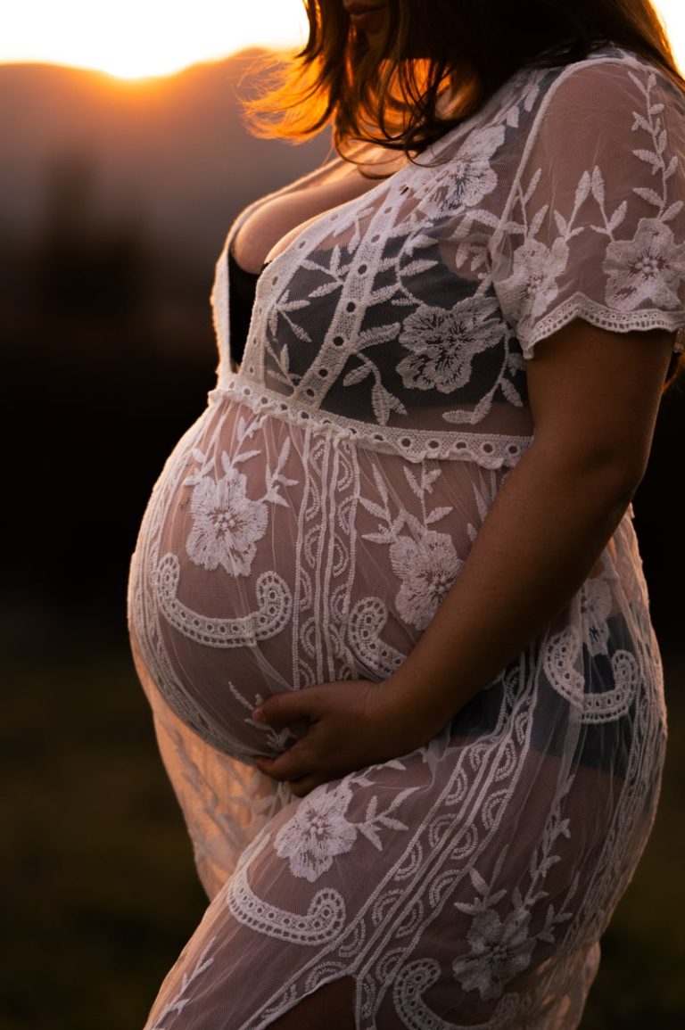 Photographie de détail d'une femme enceinte au coucher du soleil.